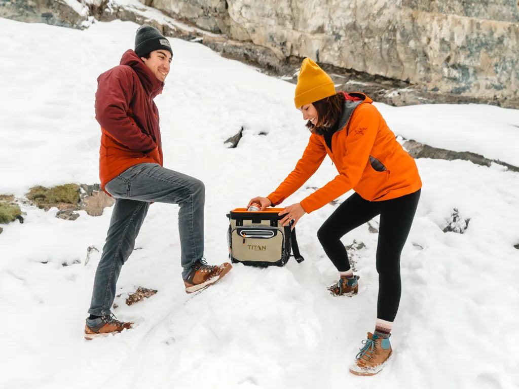 Two people outside in the snow grabbing a cold drink out of a Titan cooler